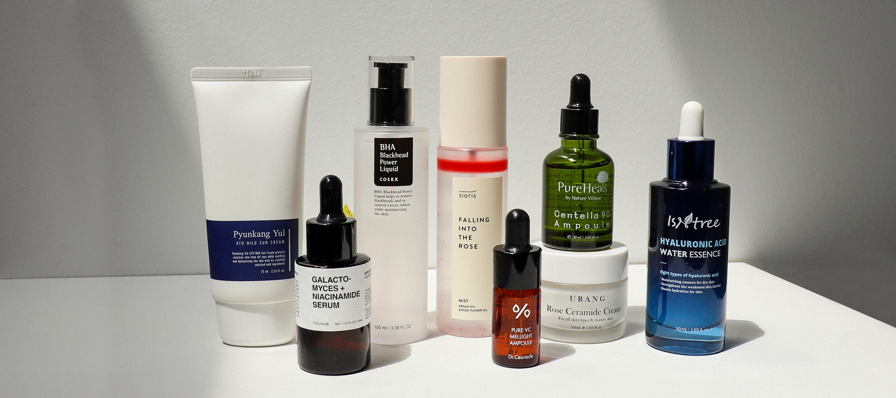 An assortment of eight various K-beauty skincare bottles and jars, including brands like COSRX and Isntree, grouped together on a plain white surface.