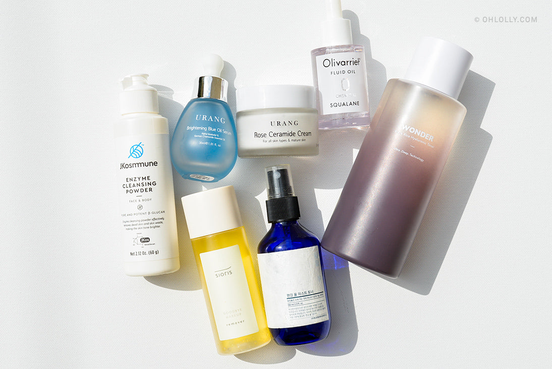 An assortment of clean beauty skincare products including bottles, droppers, and a cream jar from brands like URANG, Sioris, and Haruharu WONDER, arranged on a white surface.