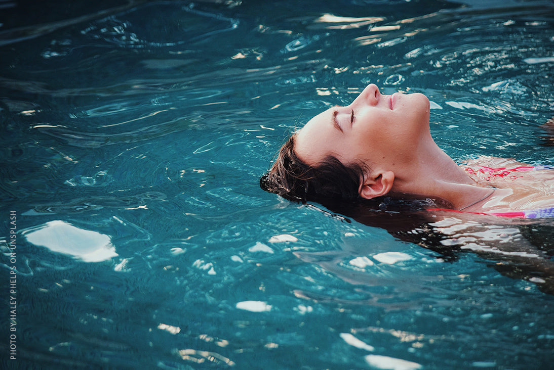 A woman floating peacefully on her back in deep blue water with her eyes closed.
