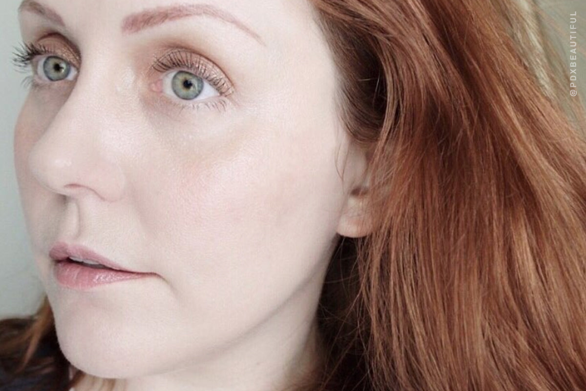Portrait of a red-haired woman with bright eyes. Overlay text: PDXBEAUTIFUL. Beauty and makeup focus.