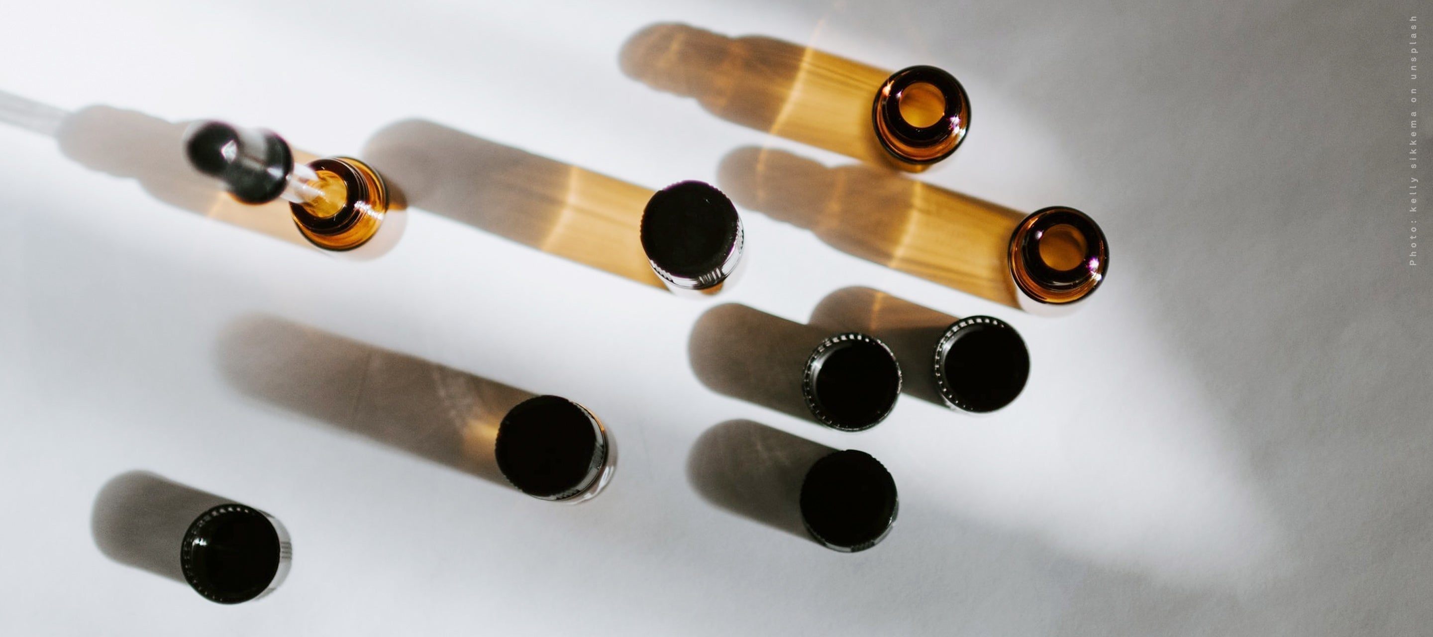 Small amber glass vials and droppers arranged on a white surface, representing essential oils, concentrated extracts, or skincare ingredients for formulation.