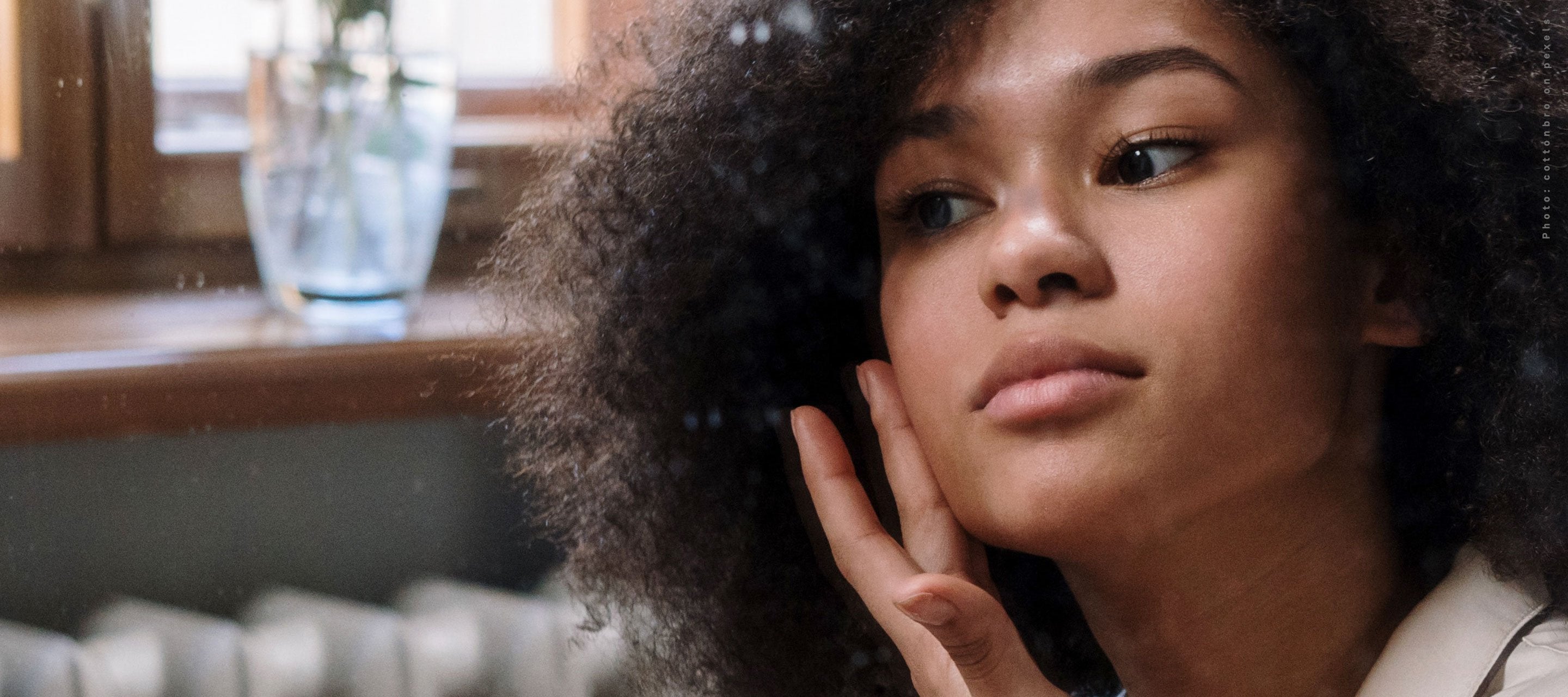 Woman with curly hair examining her skin in a mirror.