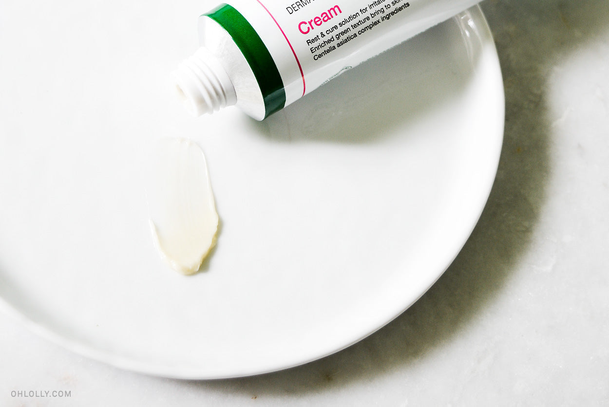 A white tube of Centella Asiatica cream squeezing a dollop of product onto a white plate.