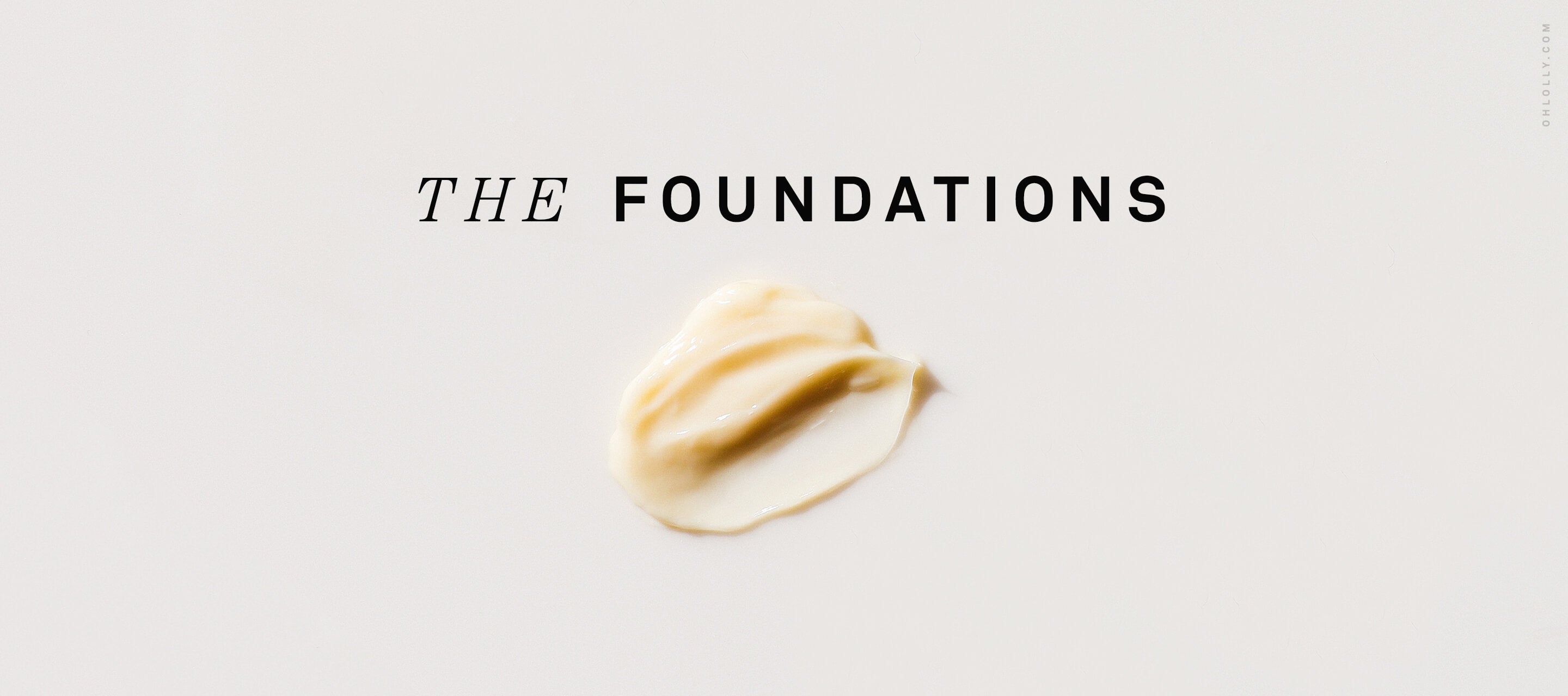 A dollop of thick, beige skincare cream centered on a light background with the words "THE FOUNDATIONS" printed in black text above it.