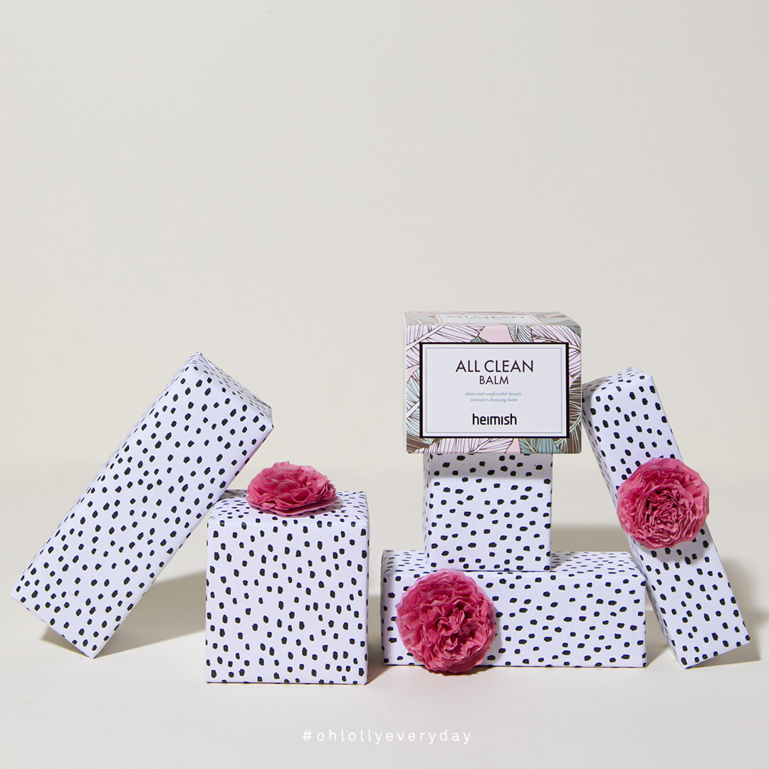 Several gift-wrapped boxes with black-and-white polka dots and pink pom-poms arranged around a box of Heimish All Clean Balm.