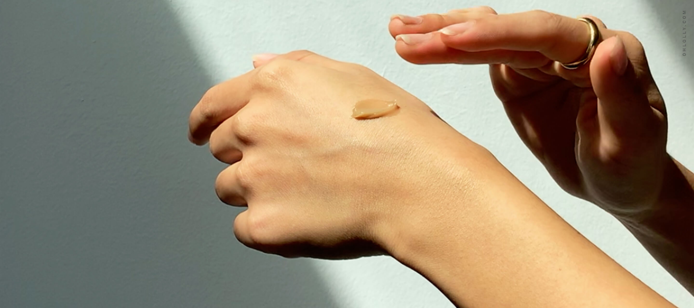 A close-up of a person's hand with a small dab of tan-colored cream applied to the back of it.