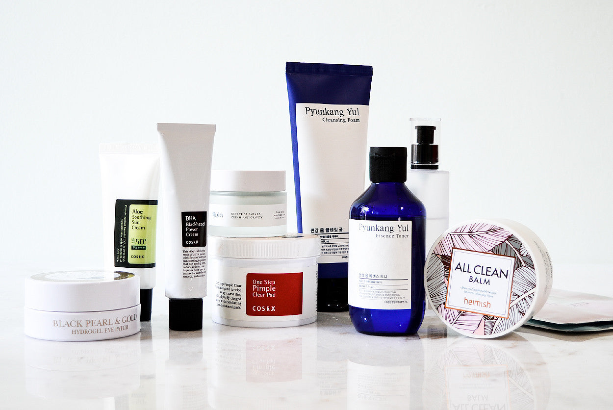 An assortment of K-beauty products, including a blue-labeled bottle and jars, lined up on a white surface.