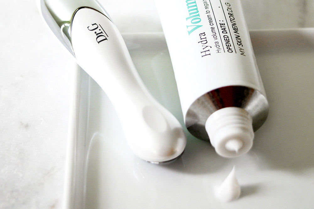 Dr. G Hydra Volume Cream dispensing product next to its handheld skincare device on a white tray.