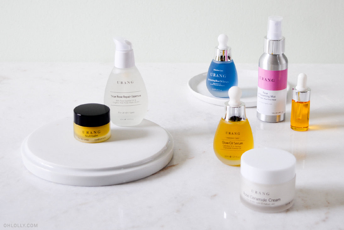 An assortment of Urang skincare products, including various oil serums in glass bottles and a white jar of Rose Ceramide Cream, on a white marble surface.