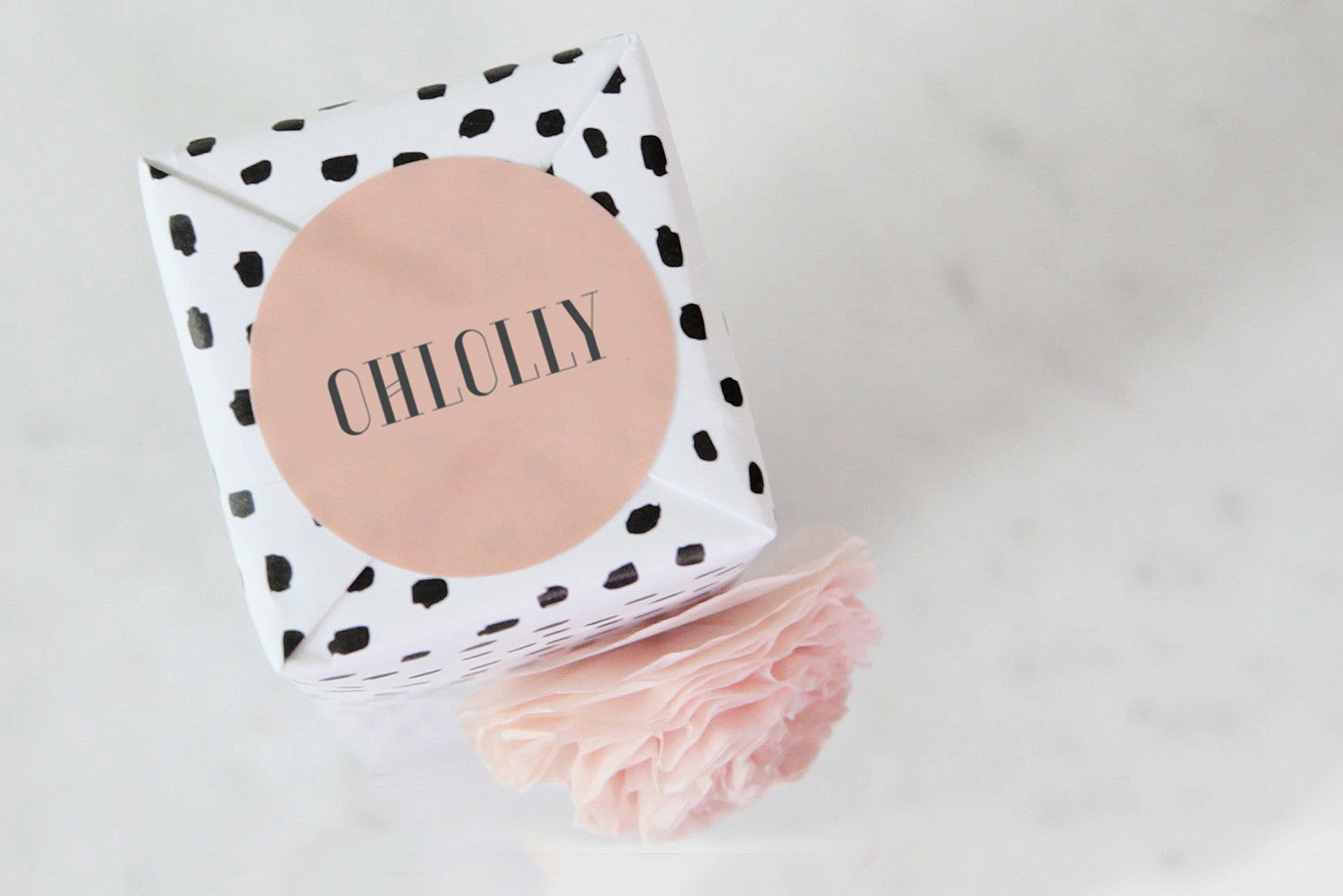 A gift wrapped in white paper with black polka dots, tied with a pink ribbon/pompom