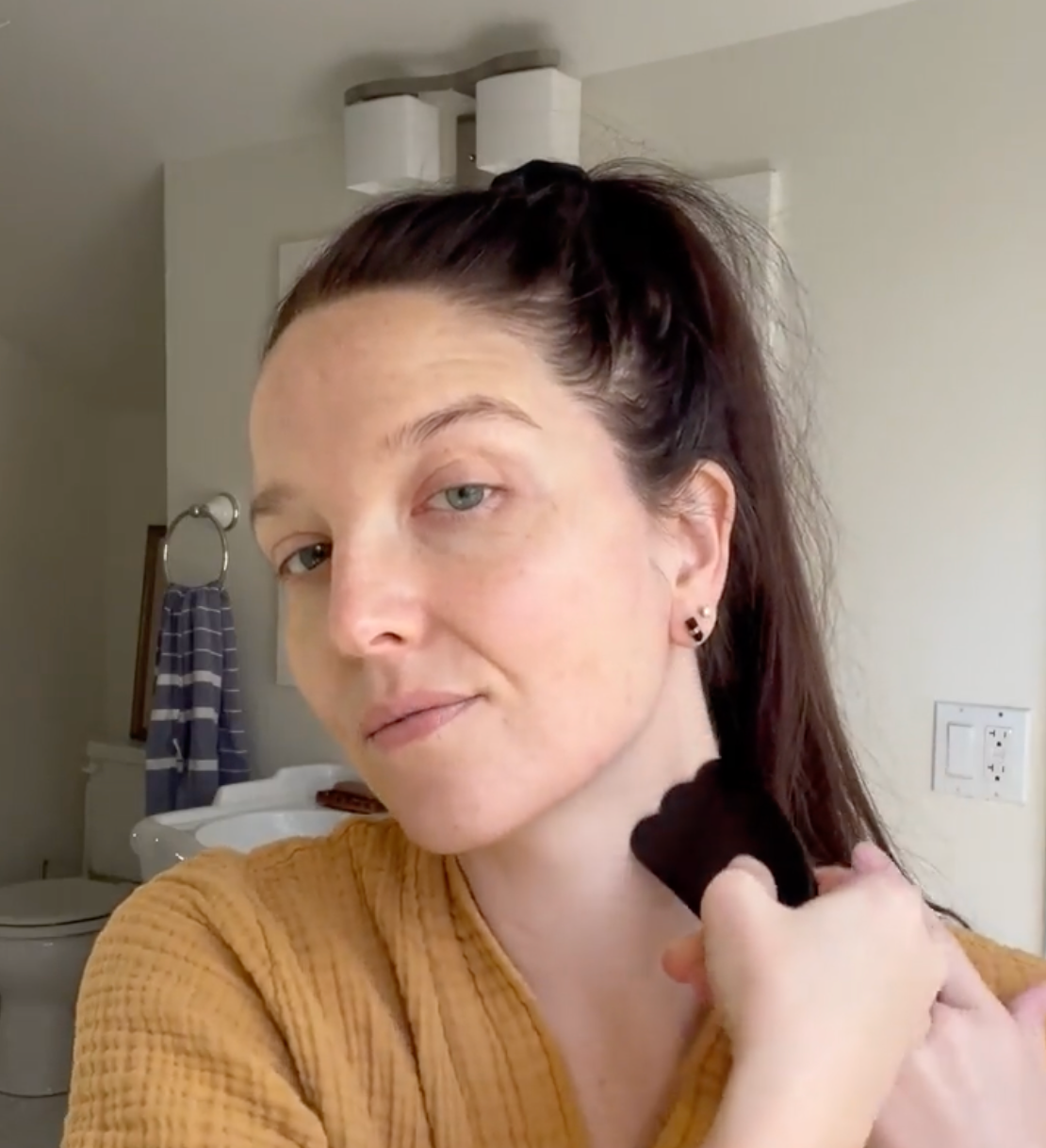 A person with their hair tied back in a ponytail uses a black, curved gua sha tool to massage the side of their neck.