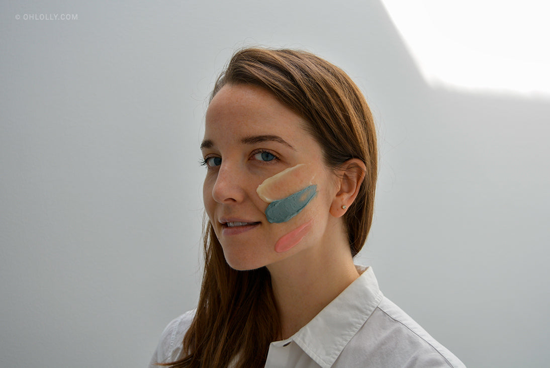 Woman with swatches of multi-colored clay masks (pink, green, beige) on her cheek. Multi-masking trend.