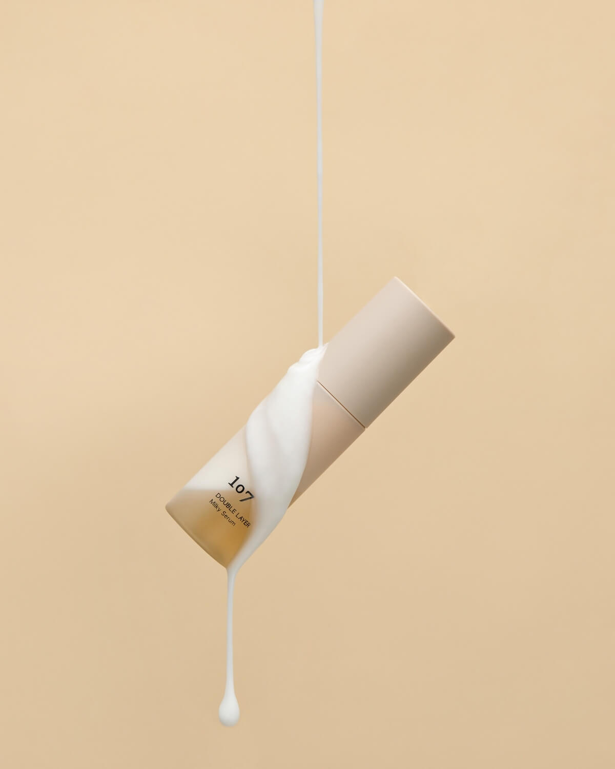 Milky white serum texture pouring over a floating bottle of 107 Milky Serum.
