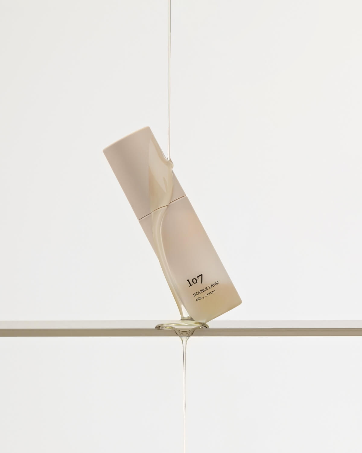 Clear hydrating liquid pouring over a bottle of 107 Double Layer Milky Serum.
