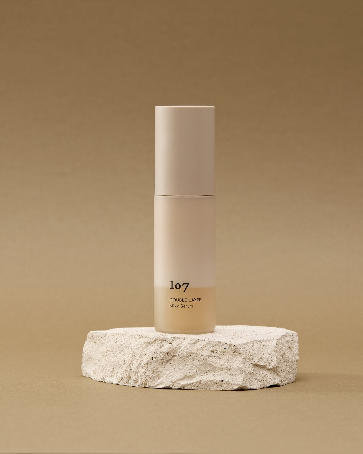 107 Double Layer Milky Serum displayed on a natural stone pedestal.