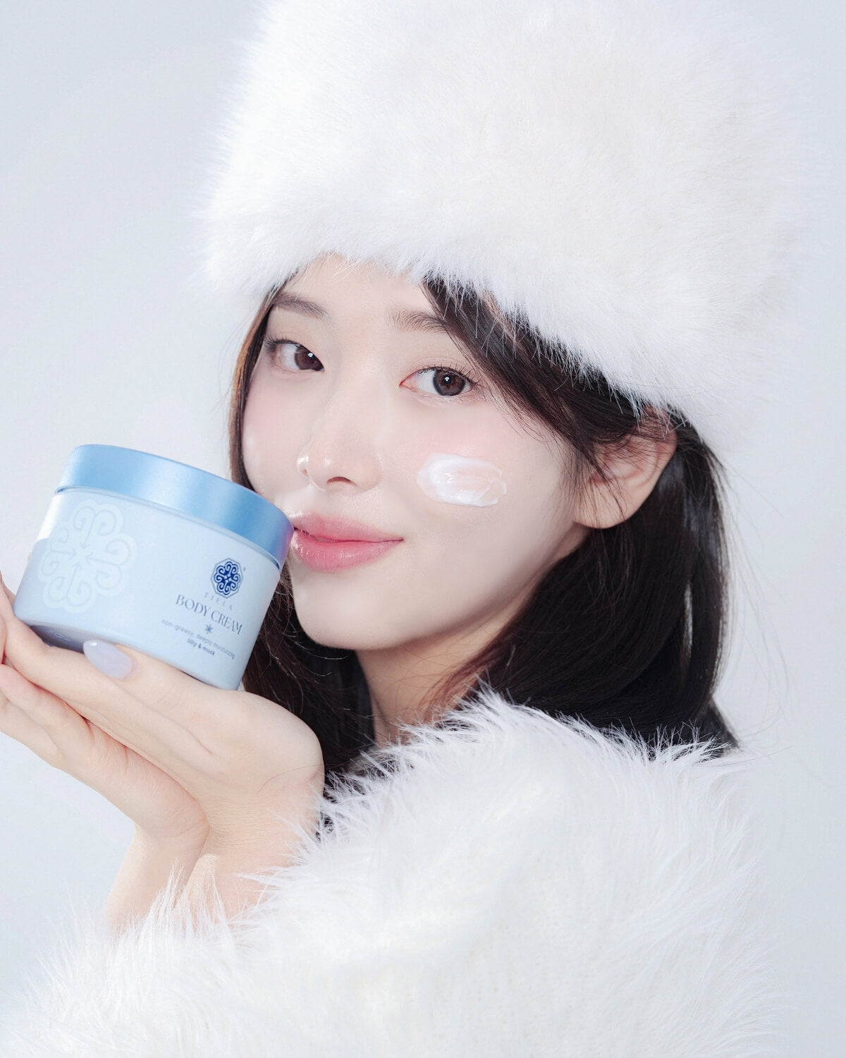 Woman in winter fur hat holding BODY CREAM jar. Moisturizing care for dry skin. Korean beauty body lotion look.