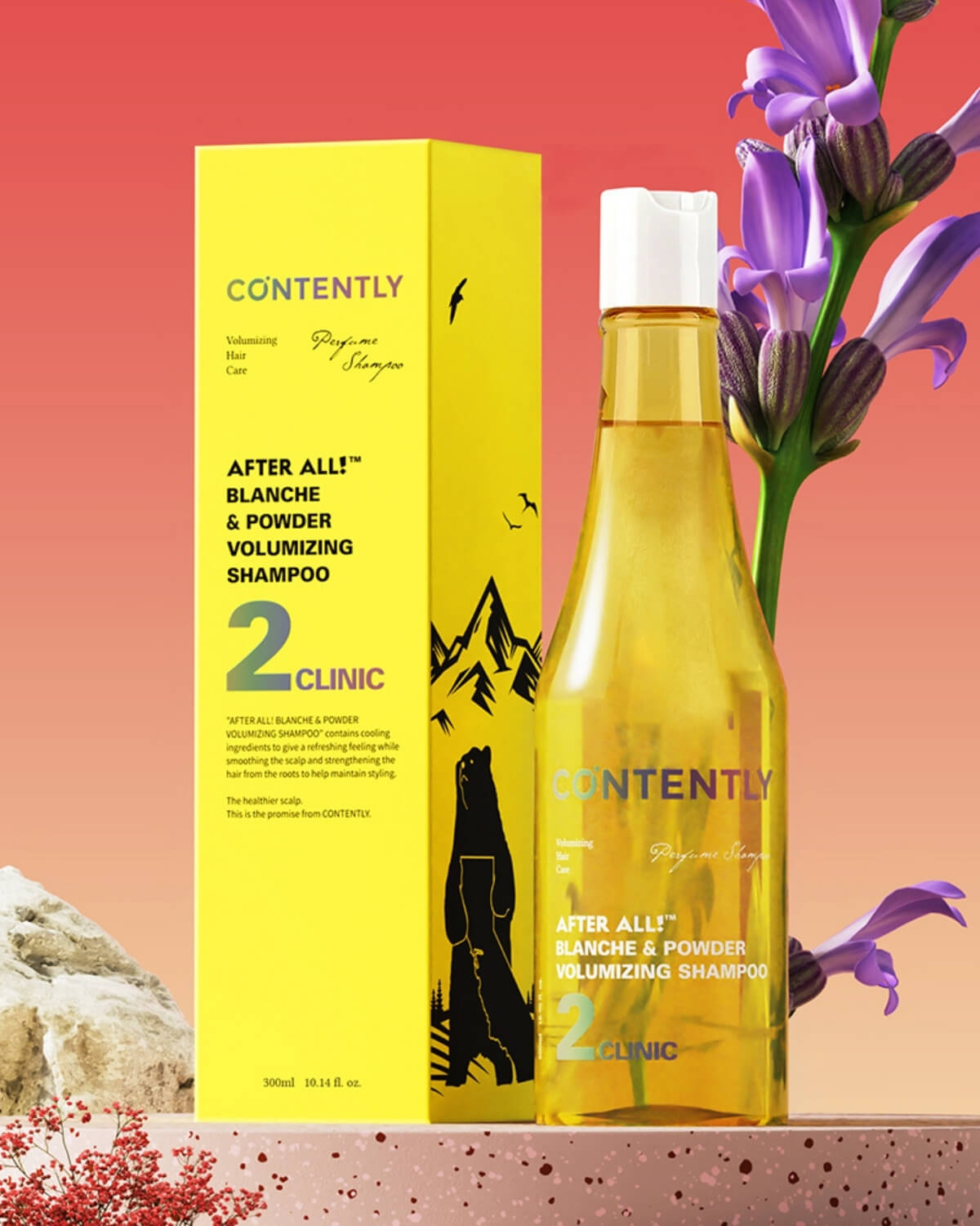 The yellow shampoo bottle stands next to its matching yellow retail box, which features mountain and bird graphics. Tall purple Agapanthus flowers are to the right, and a white rock with small red leaves is on the left, all set against a warm reddish background.