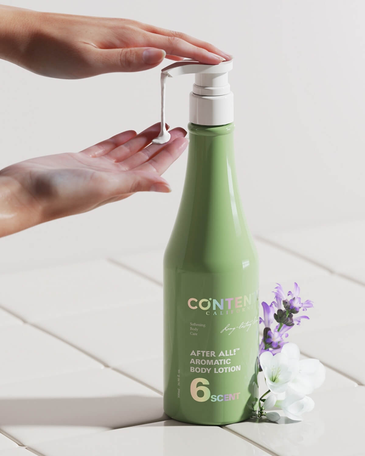 A light green bottle of the body lotion is standing on a white tile surface. A woman's hands are shown catching the white lotion product as it is pumped out of the dispenser. The base is decorated with purple lavender and a white flower.