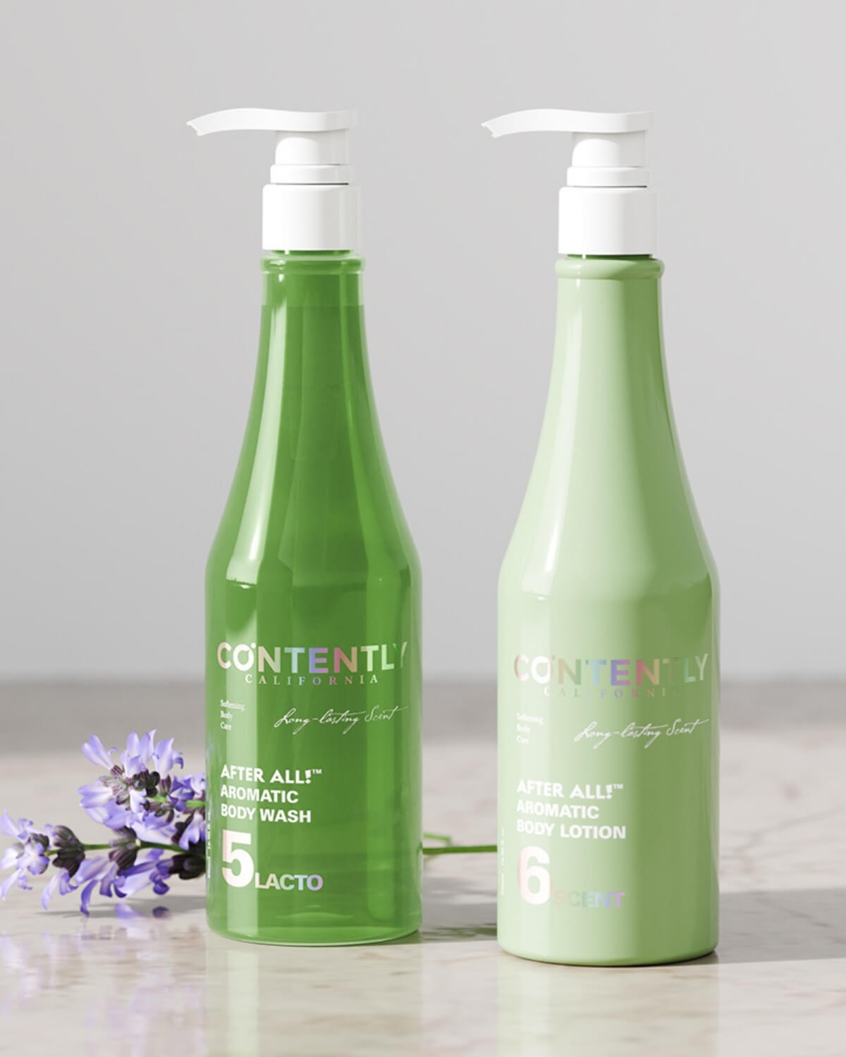 A side-by-side display of the dark green "Body Wash" bottle and the light green "Body Lotion" bottle. A sprig of purple lavender rests at the base of the two bottles on a light marble surface.