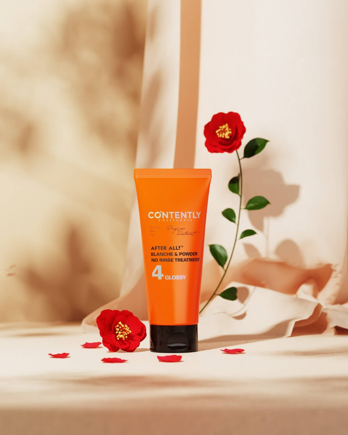 A tube of CONTENTLY CALIFORNIA's "After All!" hair treatment stands on a beige surface with a draped fabric background. A single red rose on a stem arcs over the product, with a fallen red flower and petals scattered around it.