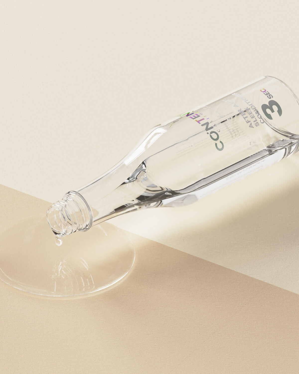 The clear conditioner bottle is lying on its side, spilling a puddle of clear liquid onto a two-toned beige surface, showing its liquid texture.