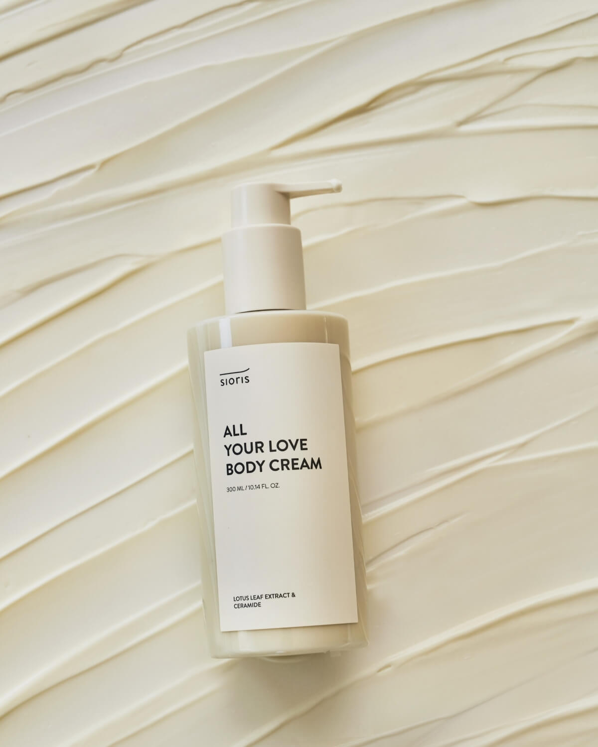 Sioris All Your Love Body Cream bottle resting flat on a thick swirl of textured ivory lotion.