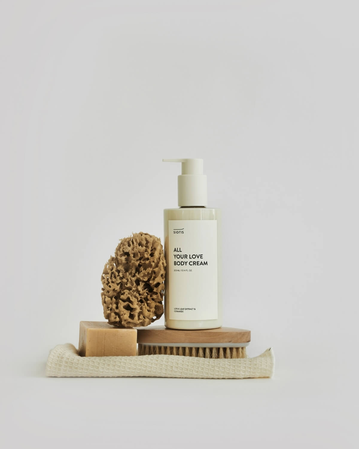 Sioris All Your Love Body Cream bottle styled on a wooden massage brush, bar soap, and waffle towel.