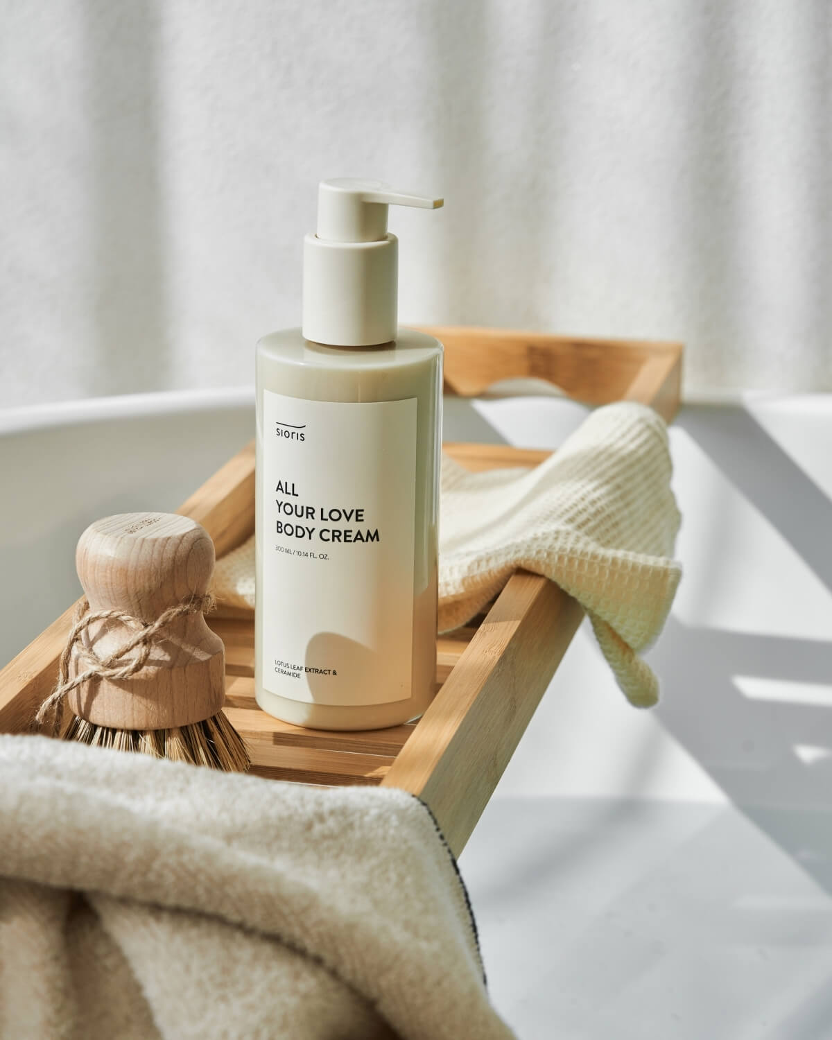 Sioris All Your Love Body Cream bottle on a wooden bath tray over a white bathtub with natural sunlight.