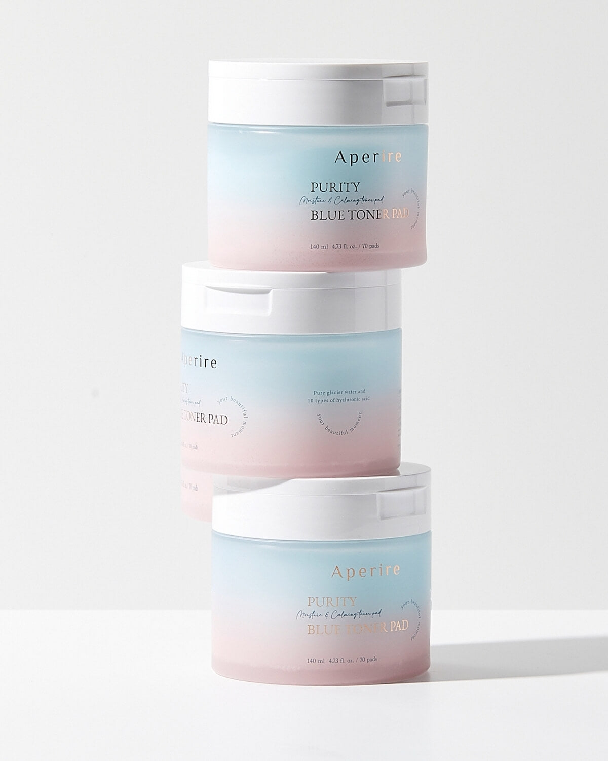 Three round containers of the Aperire Purity Blue Toner Pad are stacked vertically on a white surface, showcasing their blue-to-pink ombre packaging.