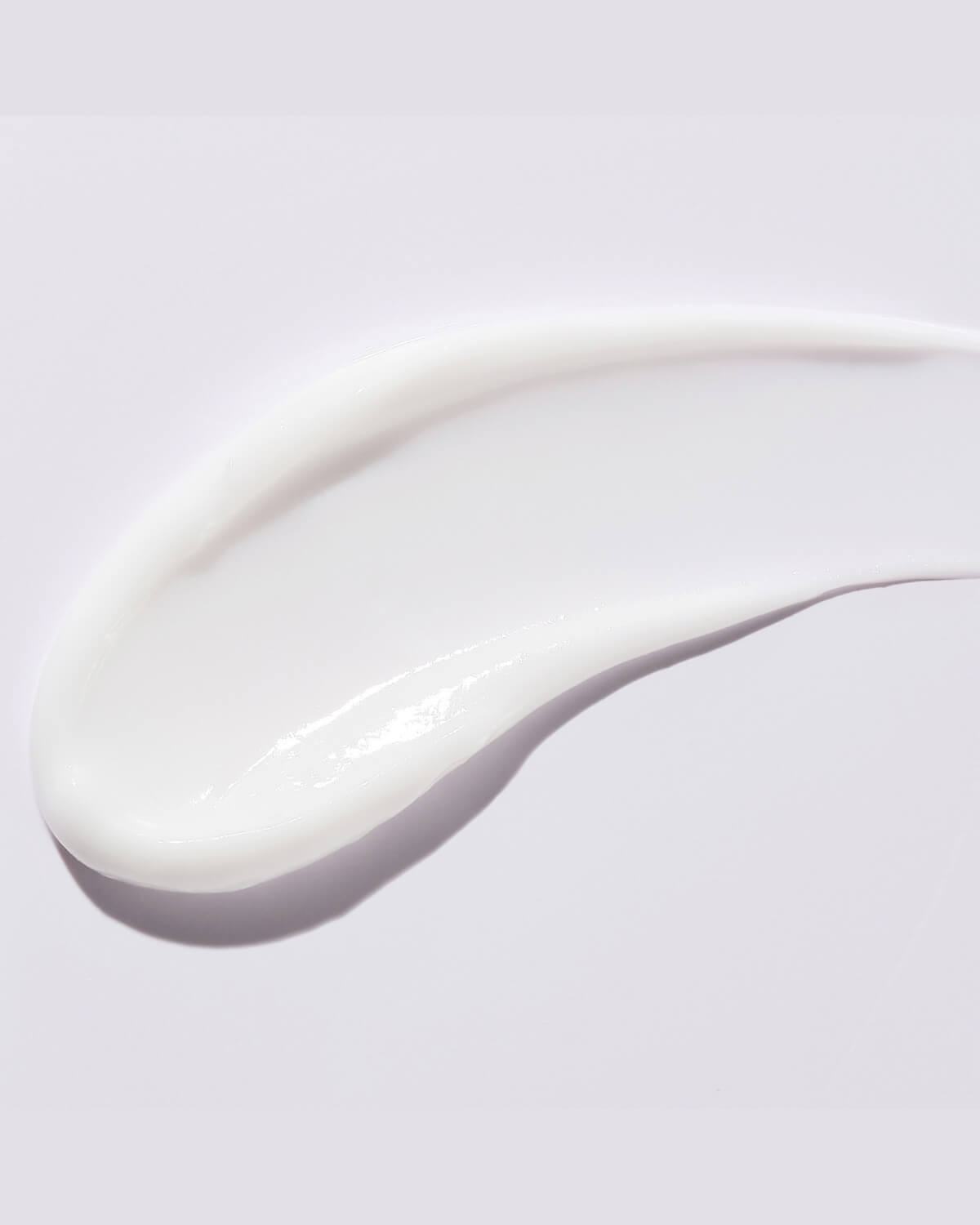 A macro shot of a smooth, thick, white swirl of cream, demonstrating the texture of the Aperire Bouncing Root Origin Cream against a plain white background.