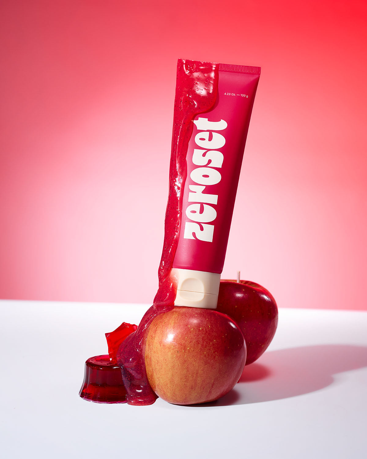 Zeroset Red Apple Jam Pack Cleanser tube coated in glossy red gel, resting on whole fresh apples and jelly.