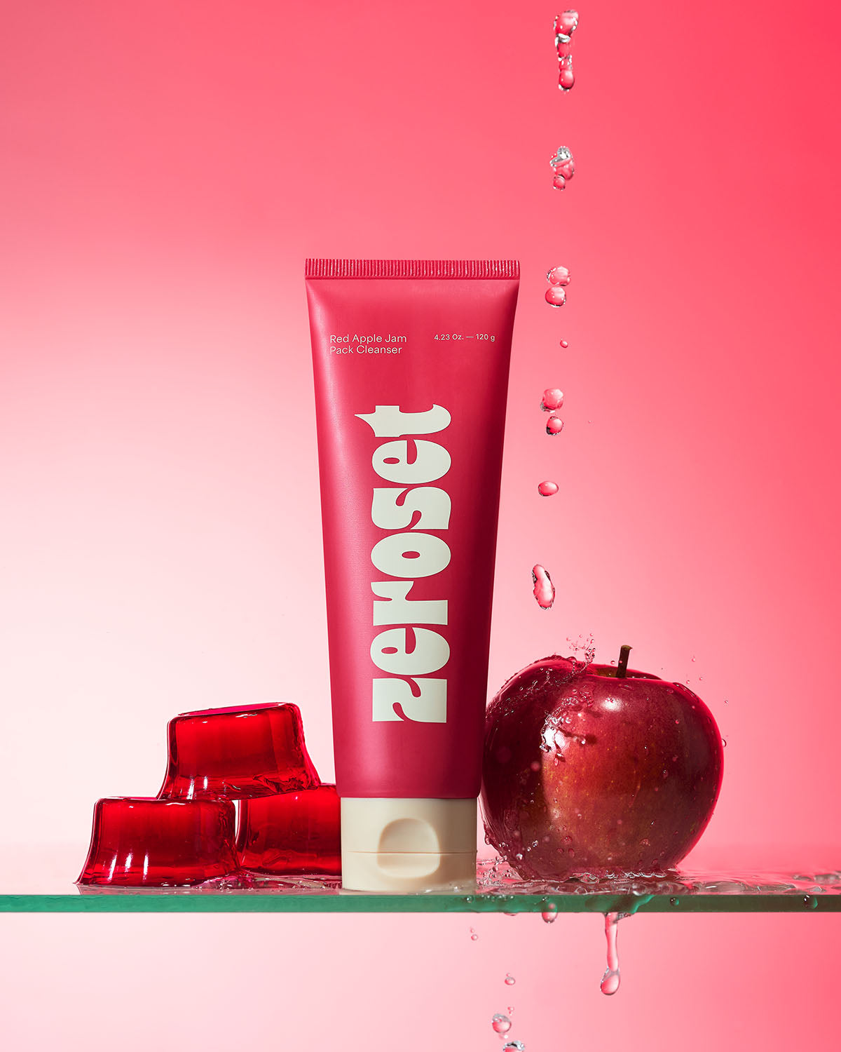 Zeroset Red Apple Jam Pack Cleanser tube standing on glass with splashing water, red apple, and jellies.
