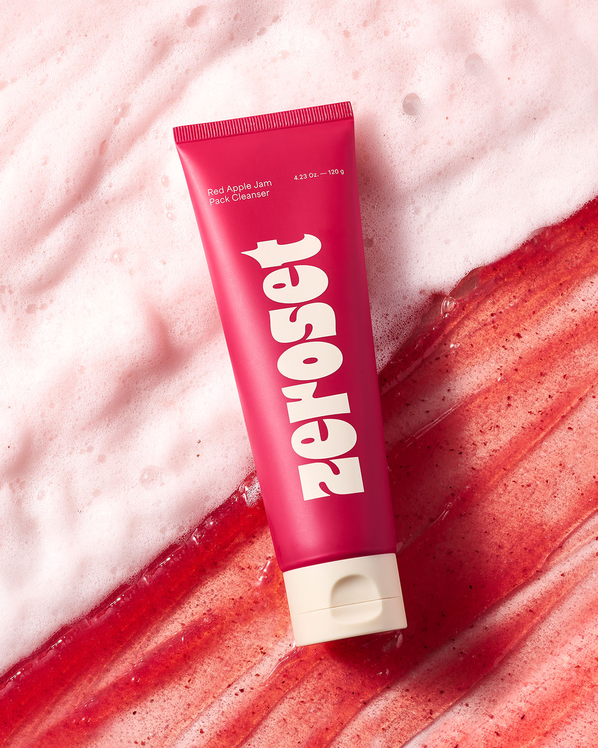 Zeroset Red Apple Jam Pack Cleanser tube lying across red exfoliating gel texture and white cleanser foam.