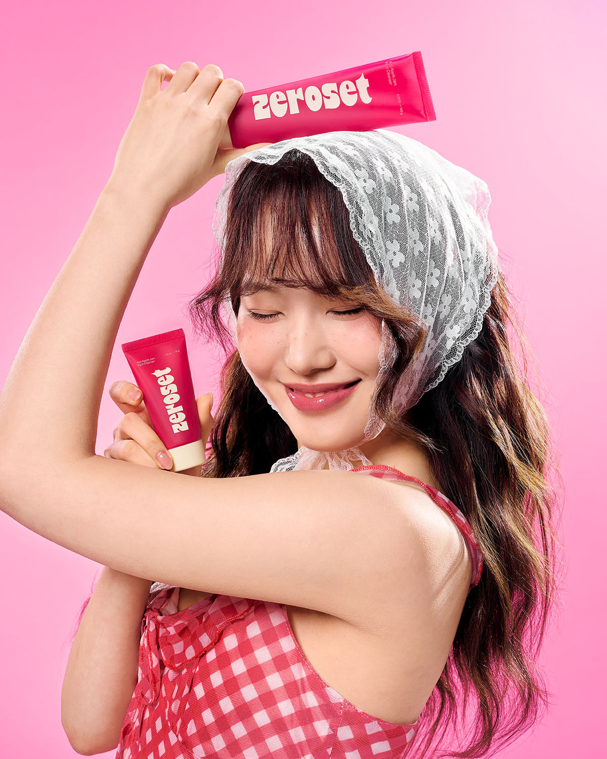 Woman wearing lace headscarf posing joyfully with two Zeroset Red Apple Jam Pack Cleanser tubes.