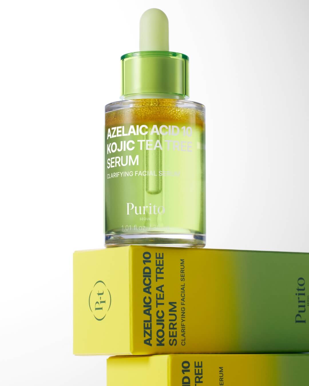 A bottle of Purito Azelaic Acid 10 Kojic Tea Tree Serum sits on top of two stacked boxes for the product. The boxes are bright yellow and green, matching the bi-phase colors of the serum in the bottle.