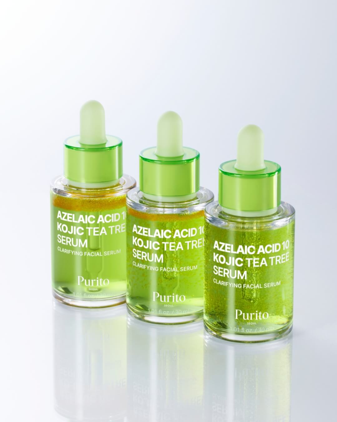 A line of three dropper bottles of Purito Azelaic Acid 10 Kojic Tea Tree Serum on a reflective surface. The bottles are slightly different, showing the two phases of the green serum in various states of separation or mixing.