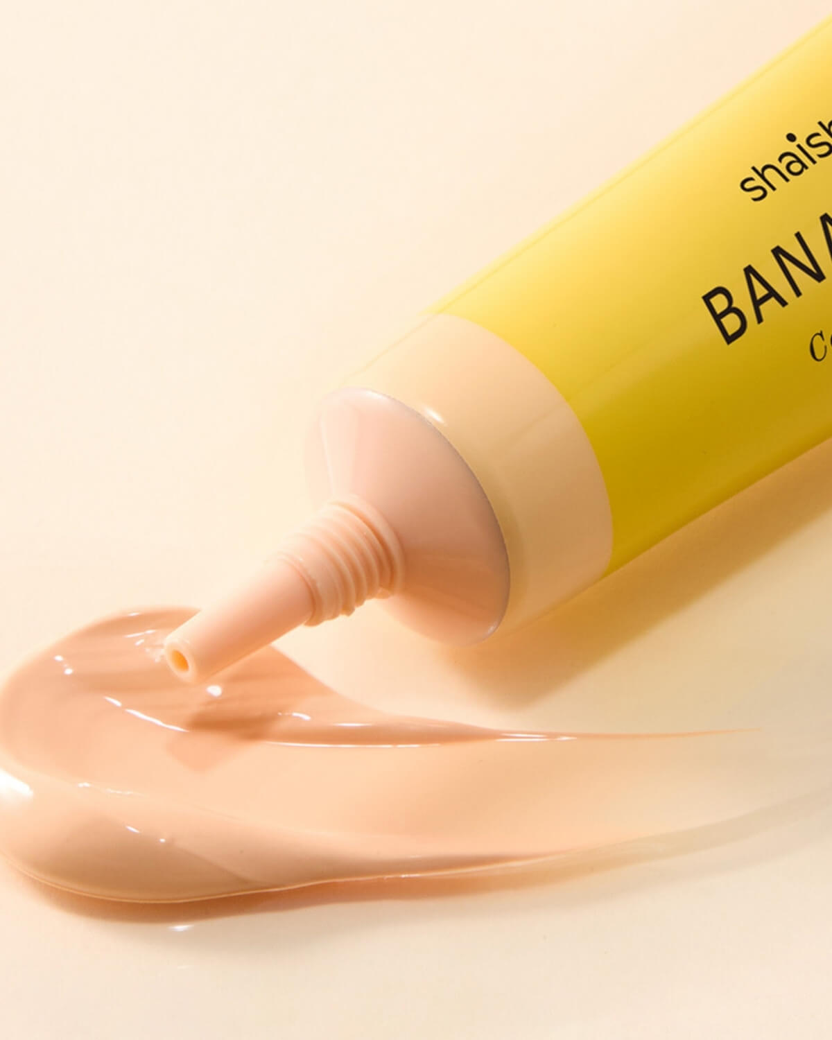 Macro shot of a creamy beige swatch of Banana PDRN Conceal Eye Cream next to the applicator tip.