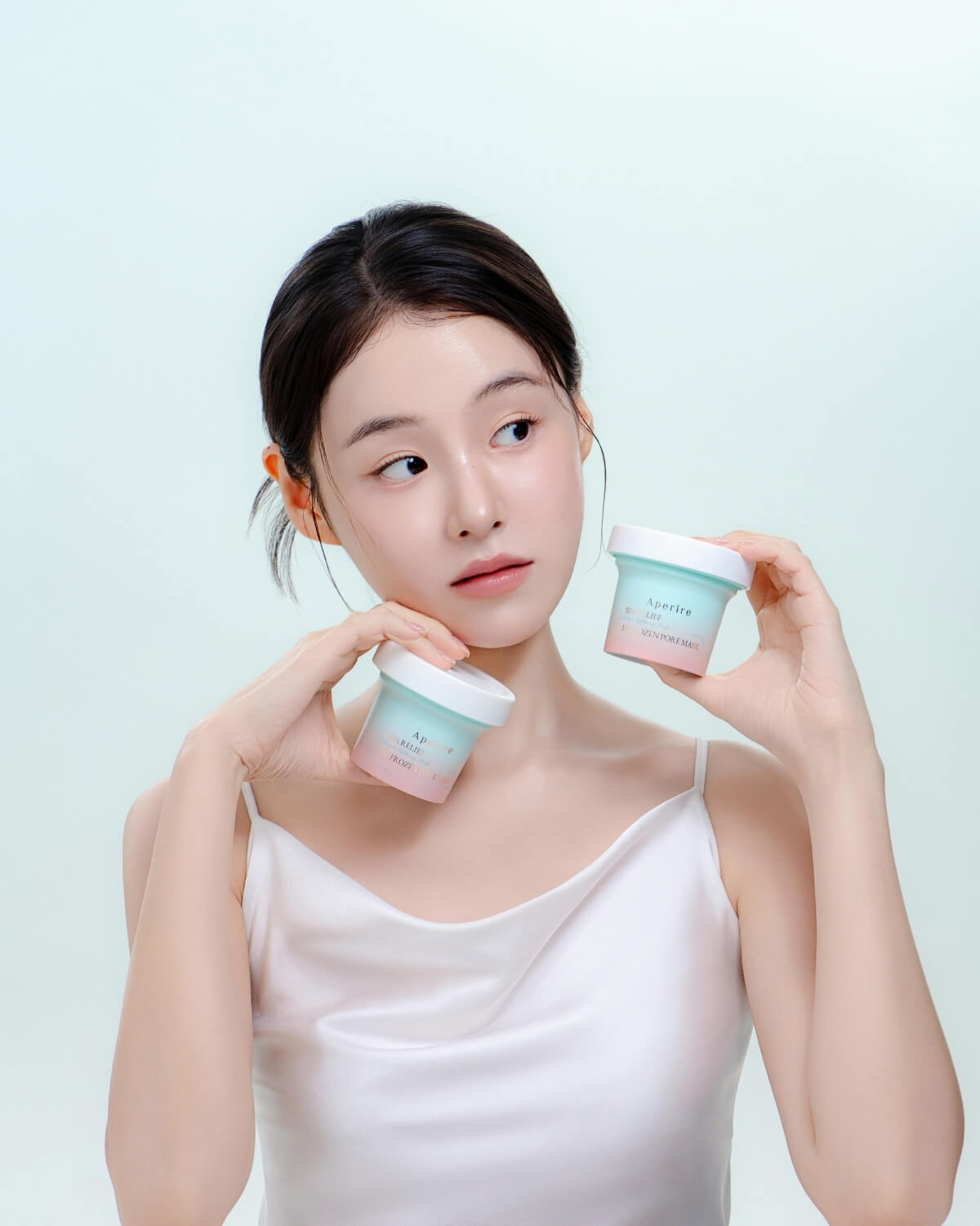 A model holds two jars of Aperire Spa Relief Be Frozen Pore Mask, showcasing the product and its cooling benefits.