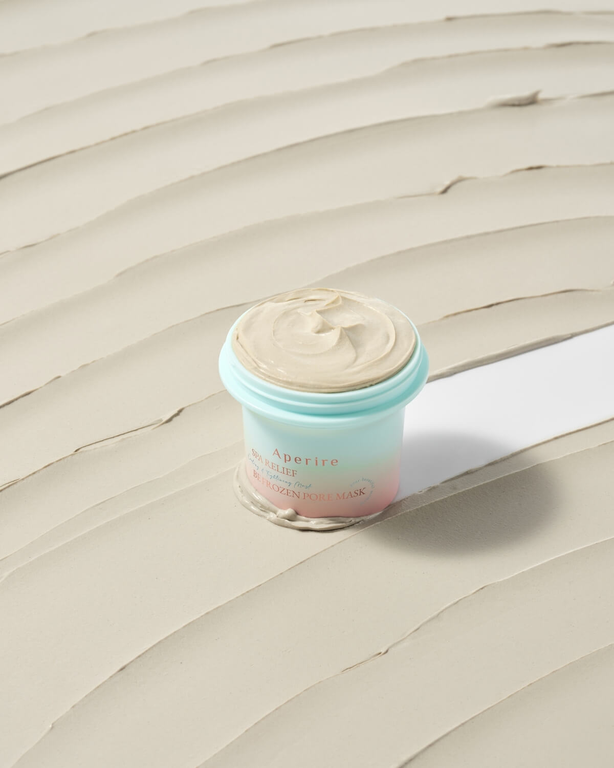 Aperire Be Frozen Pore Mask jar sitting in a smooth smear of the light beige clay product.