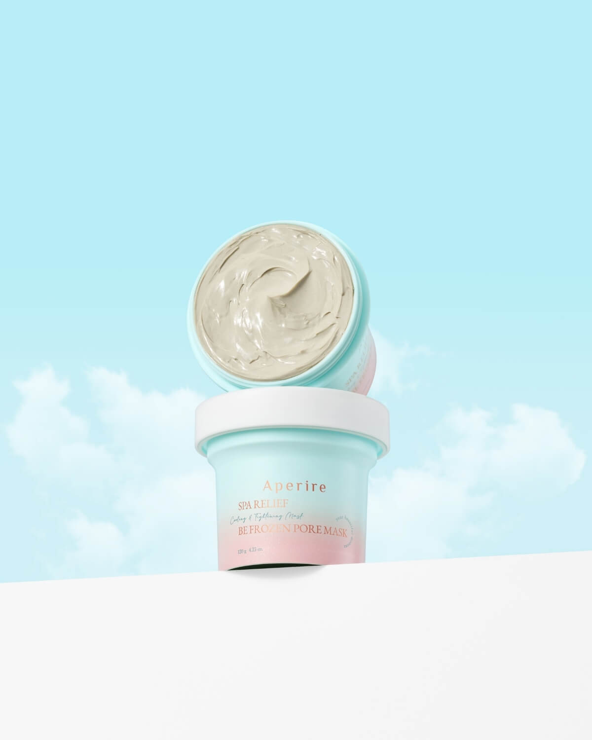 Two jars of Aperire Spa Relief Be Frozen Pore Mask, a cooling and tightening clay mask, against a blue sky.