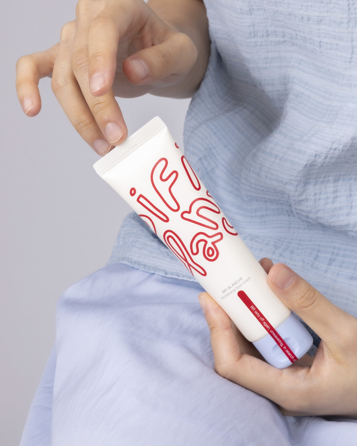 A person wearing a blue shirt holding a tube of Bifi Blanche Foot Cream with both hands.