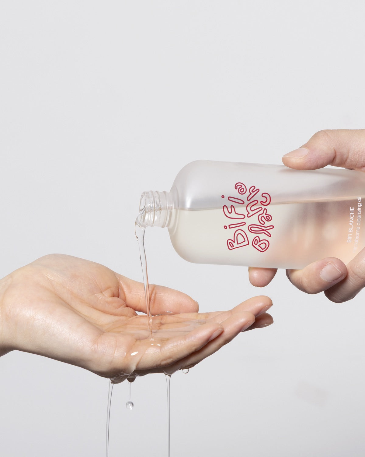 Pouring Bifi Blanche Microbiome Cleansing Oil liquid from the bottle into an open hand.
