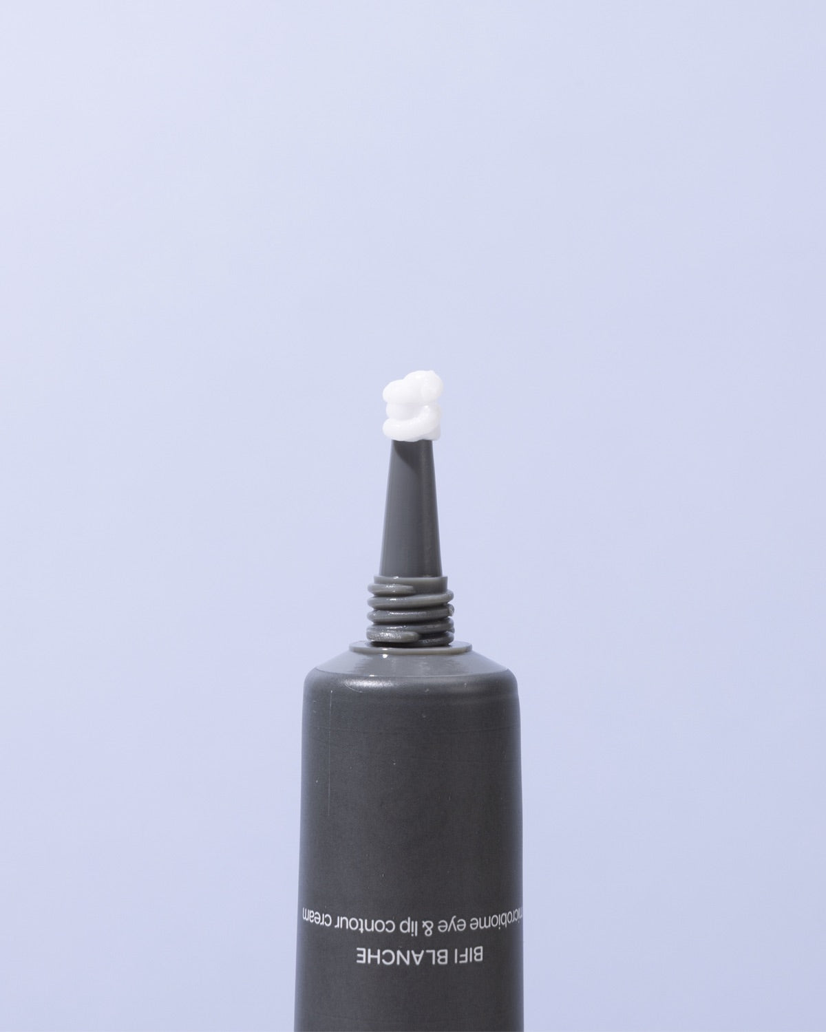 Close-up view of a white dollop of face moisturizer squeezed onto the tip of a dark gray skincare tube.