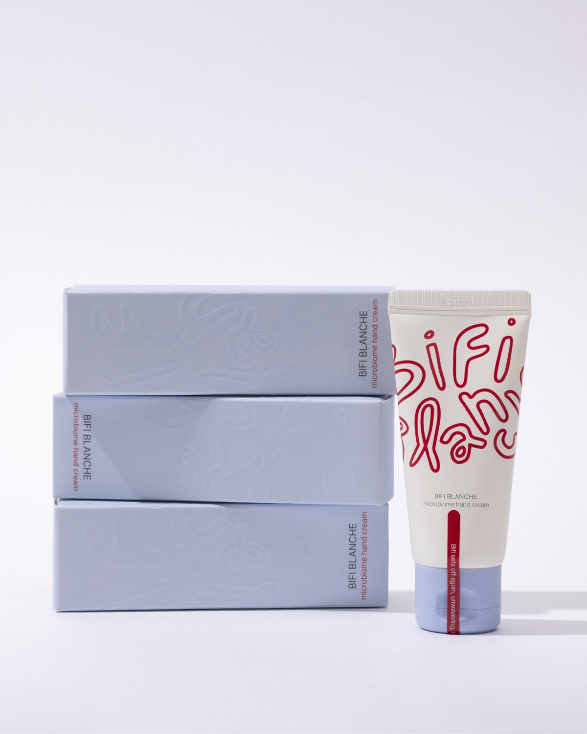 A tube of Bifi Blanche Microbiome Hand Cream standing next to a stack of three light blue product boxes.