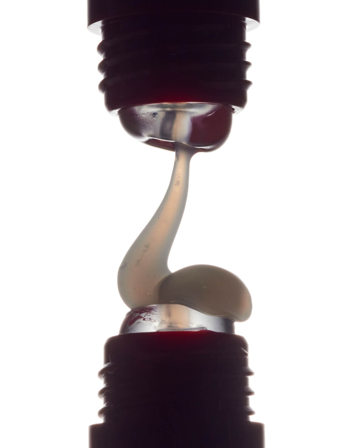 Close-up of clear, glossy lip balm texture being squeezed between two applicator tips.