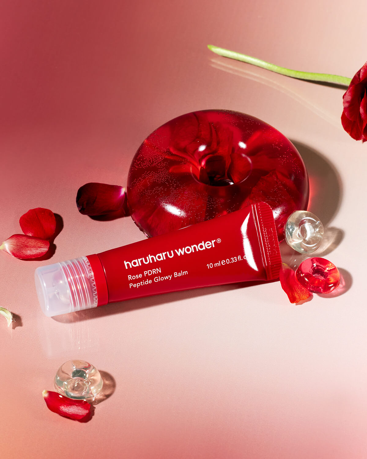 Haruharu Wonder Rose PDRN Peptide Glowy Balm on a pink surface with rose petals and glass beads.