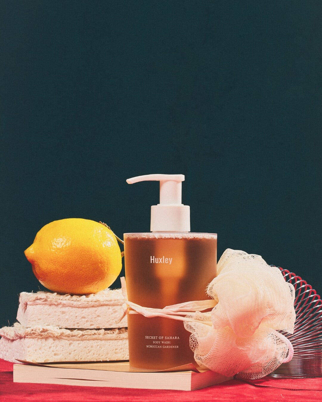 Huxley Moroccan Gardener body wash bottle styled with a fresh lemon and bath loofah.