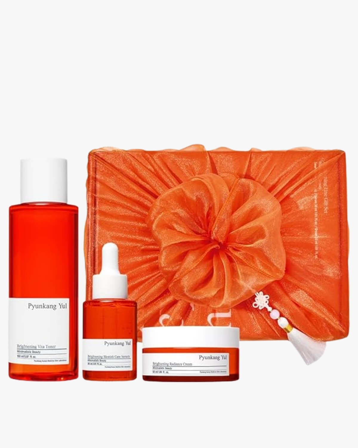 The complete Pyunkang Yul Brightening set: Vita Toner, Blemish Care Serum, and Radiance Cream, displayed next to a gift box wrapped in vibrant orange bojagi (traditional Korean wrapping cloth) with a decorative tassel.