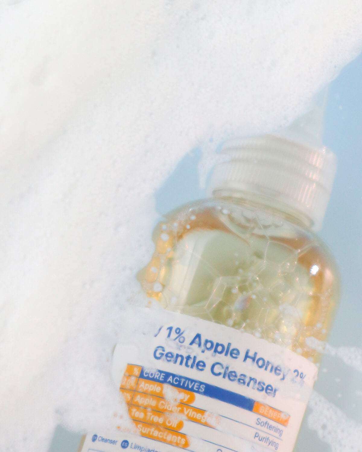 A blurred, dynamic shot of the cleanser bottle partially surrounded by white foam and suds.