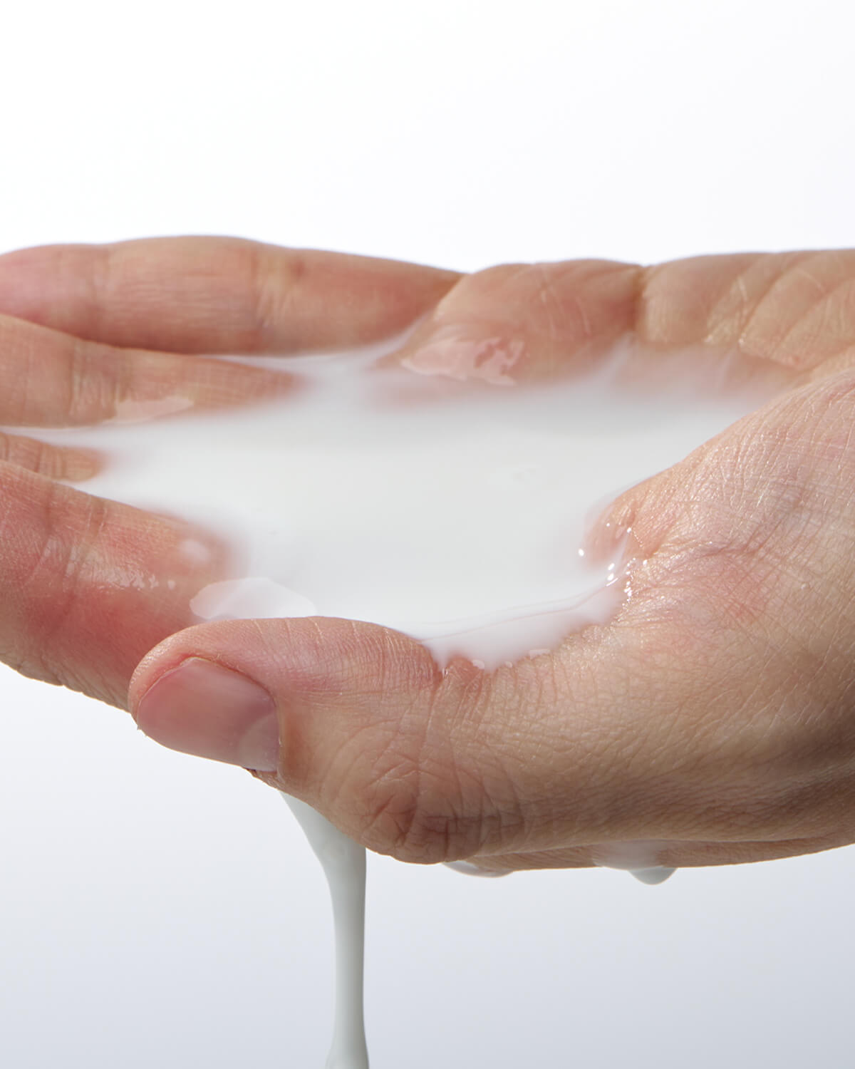 A close-up shot of a hand cupped, holding a pool of the white, milky cream, which is dripping from the palm onto a white background.